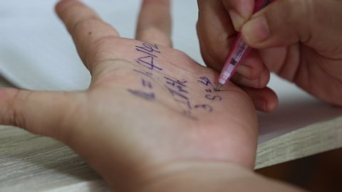 Student cheat on examination or quiz, test by using black pen to write formula of math and answers on hand. Concept of measurement and evaluation.
