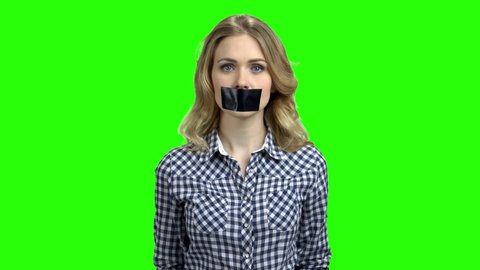 Young woman with taped mouth on green screen. Freedom of speech concept.