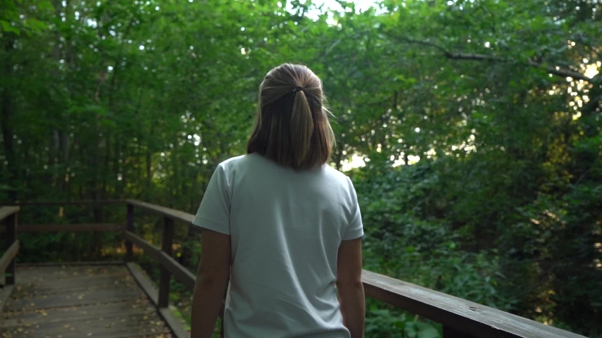 Nice slim girl in white shirt walking in woods or park forward.