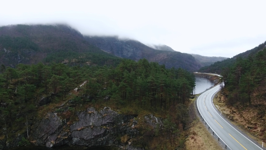 Aerial view of road in Norway with forest, lake, mountains, clouds in 4K