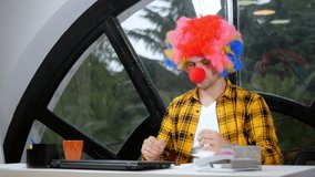 Allegory concept, office worker. Clown manager in the office. man takes off his clown’s wig and nose and starts video chat using his laptop