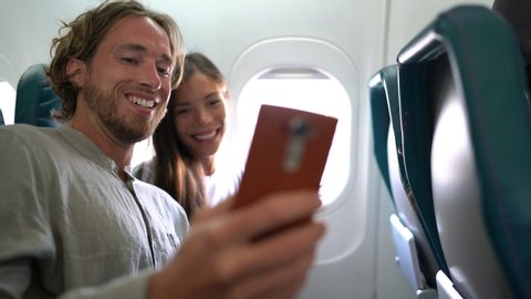 Couple in plane on travel taking selfie photo or video while flying on vacation travel. Two happy millennials taking pictures for social media going on honeymoon.