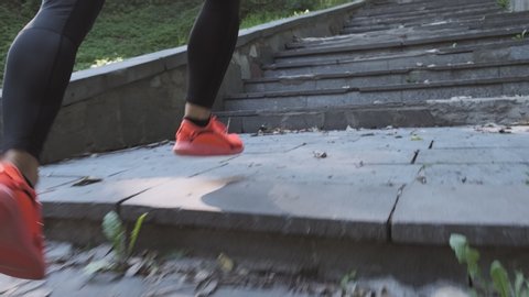 Sport man running upstairs at workout outdoor in park. Man climbing stairs at morning run in summer park. Close-up of legs with orange running shoes with copyspace. Follow shot
