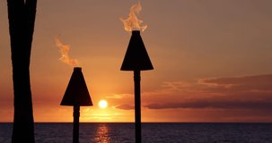 Hawaii sunset with lit tiki torches with flames. Hawaiian icon, lights burning at dusk at beach resort or restaurants for outdoor lighting and decoration, cozy atmosphere. 59.94 FPS slow motion.