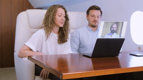 Making video conference call with colleague on laptop HUD hologram on board of private jet. Flight attendant offer glass of wine for caucasian businessman and businesswoman inside business airplane