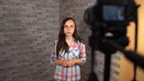 A young woman in a plaid shirt is talking on camera on a brick background. A happy woman are speaking in front of camera for vlog.