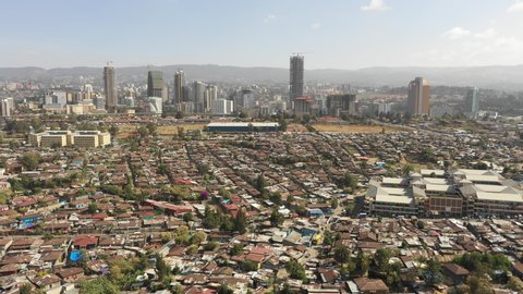 Retreating aerial footage flying over low-rise residential neighborhoods contrasting with commercial office towers and skyline Addis Ababa, changing urban landscapes Ethiopia Africa
