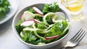 Dressing salad with olive oil. Healthy vegan or vegetarian raw salad with cucumber, kale, radish and zucchini