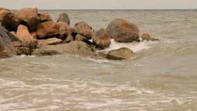 Rocks on beach in the afternoon sun, sea breeze in the air, golden sand beach, long flat waves, side view of the beach. Beautiful beach and sea. Colorful Ocean Wave. Sea water 