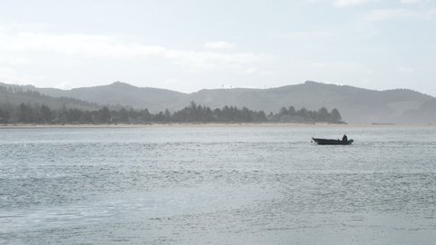Person on small fishing boat trolling solo in large bay on the Oregon Coast on hot, summer day.