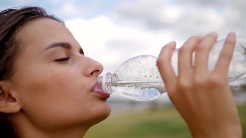 Woman drinking water from bottle after gym after working out, outdoor sport brunette girl latina drink clear mineral water after training