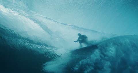 Amazing underwater shot of a blue barreling wave with the silhouette of a surfer in the barrel riding in slow motion