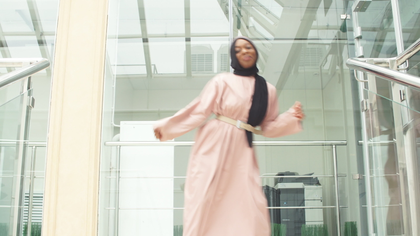 Two positive muslim young women dancing on the stairs in modern business center.