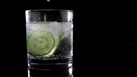 A 30 fps slow motion video of a making of gin tonic alcoholic summer cocktail with copy space and black background. The drink is in focus and well-lit