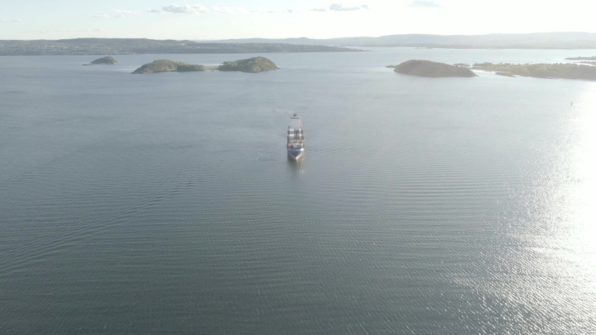 4K aerial video with birds eye view of a cargo ship with smoking polluting pipe loaded with containers outside of an International maritime container port harbor in the Oslo fjord in Oslo, Norway.