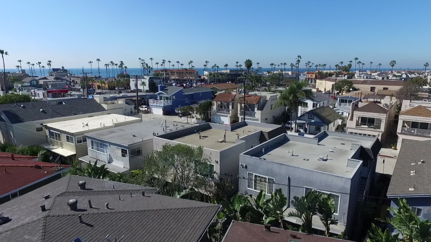 Aerial drone facing Pacific Ocean, flying over Balboa Peninsula homes, Newport Beach Pier, and businesses in Newport Beach, Orange County, California