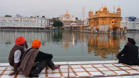 AMRITSAR, INDIA - MARCH 18, 2019: three sikh men sit by the sacred pool at golden temple in amritsar, india- 4K 60p