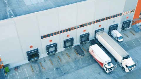 Aerial view of a semi-trailers trucks standing at the warehouse ramps for load/unload goods in the logistics park 