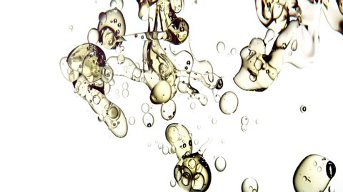 Close up and slow motion of clear gold liquid pouring into water from right side transforming into large bubbles floating on white background