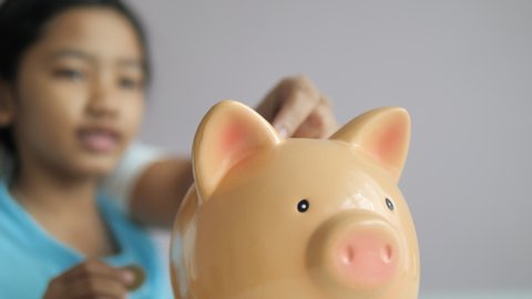 Close-up little Asian girl putting coin into the piggy bank metaphor saving money for better future select focus shallow depth of field
