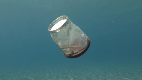 Plastic pollution in the Oceans. White plastic cup with a red lid floats beneath a surface in blue water in Mediterranean Sea, Europe. Plastic garbage environmental pollution problem. 