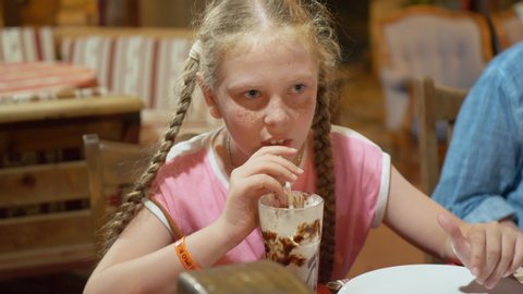 Freckled redhead girl drinking milk shake at restaurant table. Young girl teenager drinking milk chocolate cocktail while lunch in cafe