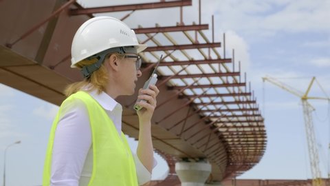 woman foreman talking on walkie-talkie at construction site. manager with radio set on background of construction of car overpass.