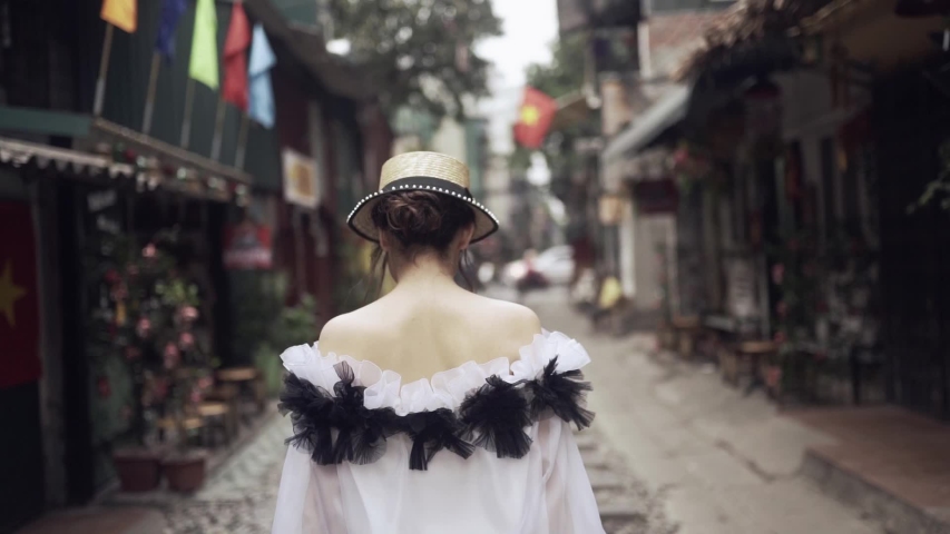Back follow view to the beautiful and young fashion girl walking along the asian street with railway between old buildings. Journey concept in Vietnamese tourist destination in Hanoi. 