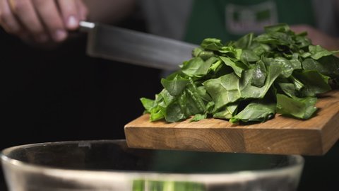 The cook pours chopped spinach from the cutting wooden board to the glass bowl, making the vegetable salad, cooking with greens, vitamin and healthy food, vegetarian meals, Full HD Prores 422 HQ