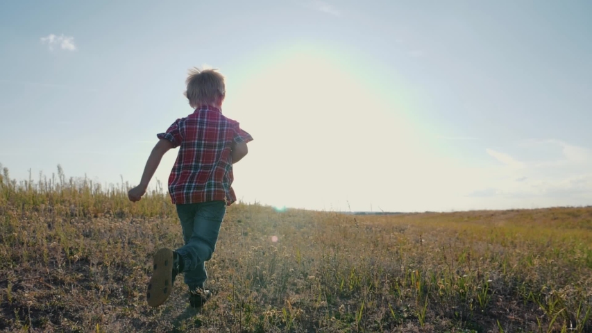 Happy boy runs on a green field in the sun at sunset. Children