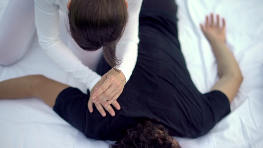 Overhead of young man guy lying facedown while his back and shoulders being massaged by a Shiatsu masseuse. Backache. Shiatsu treatments for healthy life wellbeing. Cine lens. Royalty-Free Stock Footage #1035899225