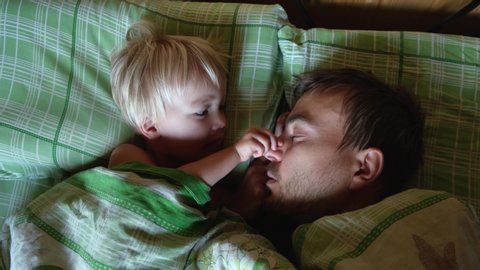 Cute toddler son and father sleeping together on bed in bedroom at home, little boy wake up their dad.