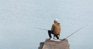 grandfather sits on the pier and catches fish from the river