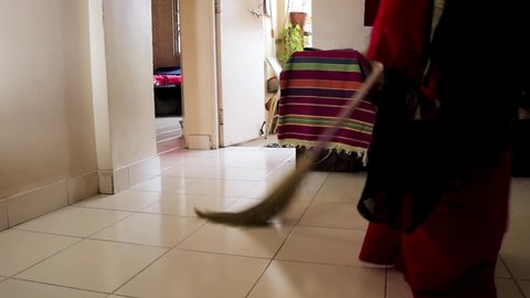 Indian saree women sweeping / cleaning her house Hall, cleaning housework and housekeeping concept - asian woman with broom sweeping floor. a Close-Up of Young Woman sweeping in black red saree.