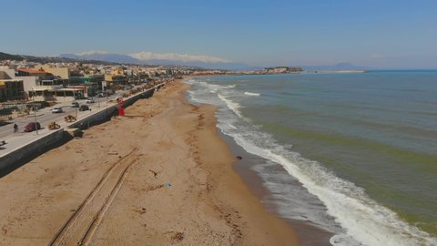 Aerial footage above the beach in Rethymno (Ari Velouchioti street) in Crete, Greece during the Winter when the beach is empty of sunbeds.