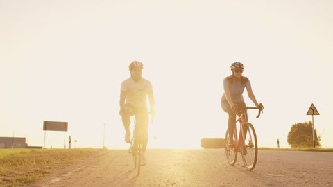 A man and a woman on bicycles ride down the road at sunset together in slow motion. The couple travels by Bicycle. Sports Cycling helmets