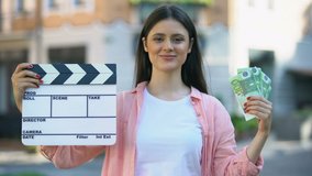 Woman showing clapperboard and bunch of euros at camera, film production worker
