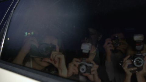 Celebrity couple in car hiding with hand from magazine photographers cameras