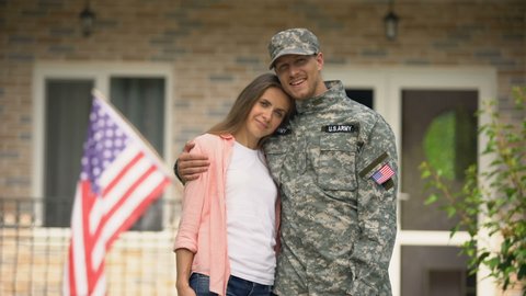 Former soldier and girlfriend hugging, standing against USA flag, homecoming