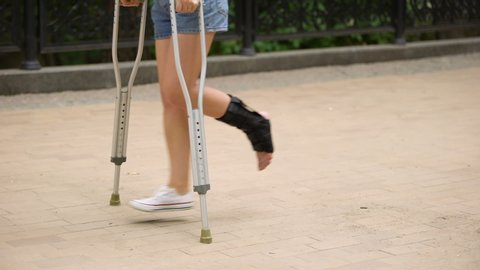 Woman with injured ankle walking on crutches outdoors, leg strain, fracture