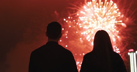 Happy couple in love looking at the sky and enjoys the party. Silhouette of people watching explosive and colorful fireworks in the evening sky. Holiday event and celebration. People have fun.