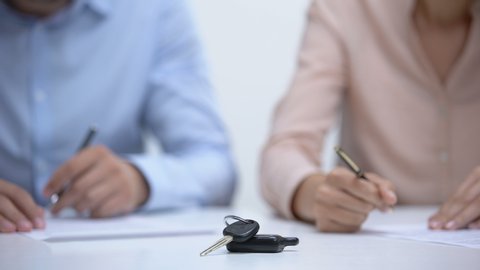 Car keys closeup, couple signing divorce documents about property division