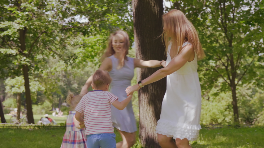 Two young women and their little children spinning on the lawn holding hands