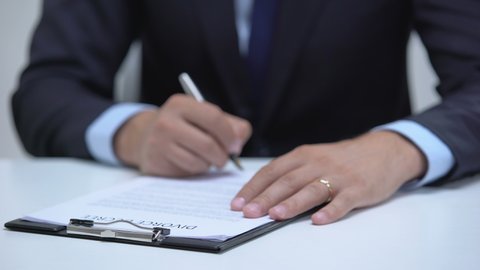 Man signing divorce decree, angrily taking off wedding ring, property division