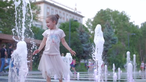 Happy little girl in the city playing with water in fountains, happy and carefree childhood, the concept of freedom and happiness in childhood, summer vacation.