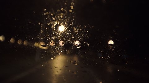 Rain drops on car windshield. Abstract street lights in the background. Night driving.
