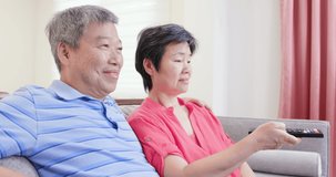 eldely couple sit on the sofa and watch tv happily with remote control