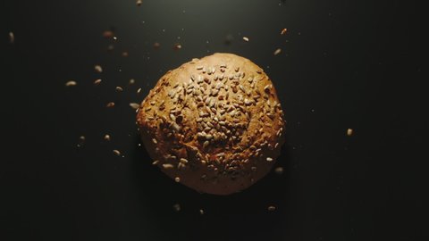 SLOW MOTION: Round Loaf Of Bread With Seeds Falling Down On A Black Surface
