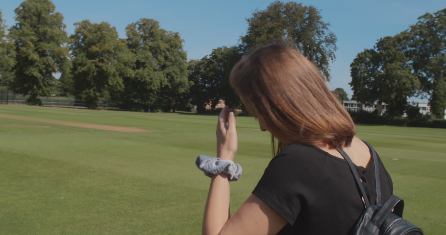 A HANDHELD SHOT of a woman walking through a park on a sunny day. SLOW MOTION.