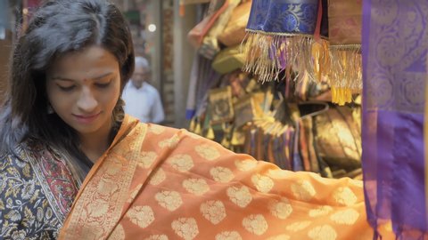 An attractive happy woman talking with the shopkeeper and choosing from the various ethnic sarees or traditional clothes displayed at the shop during the festival 